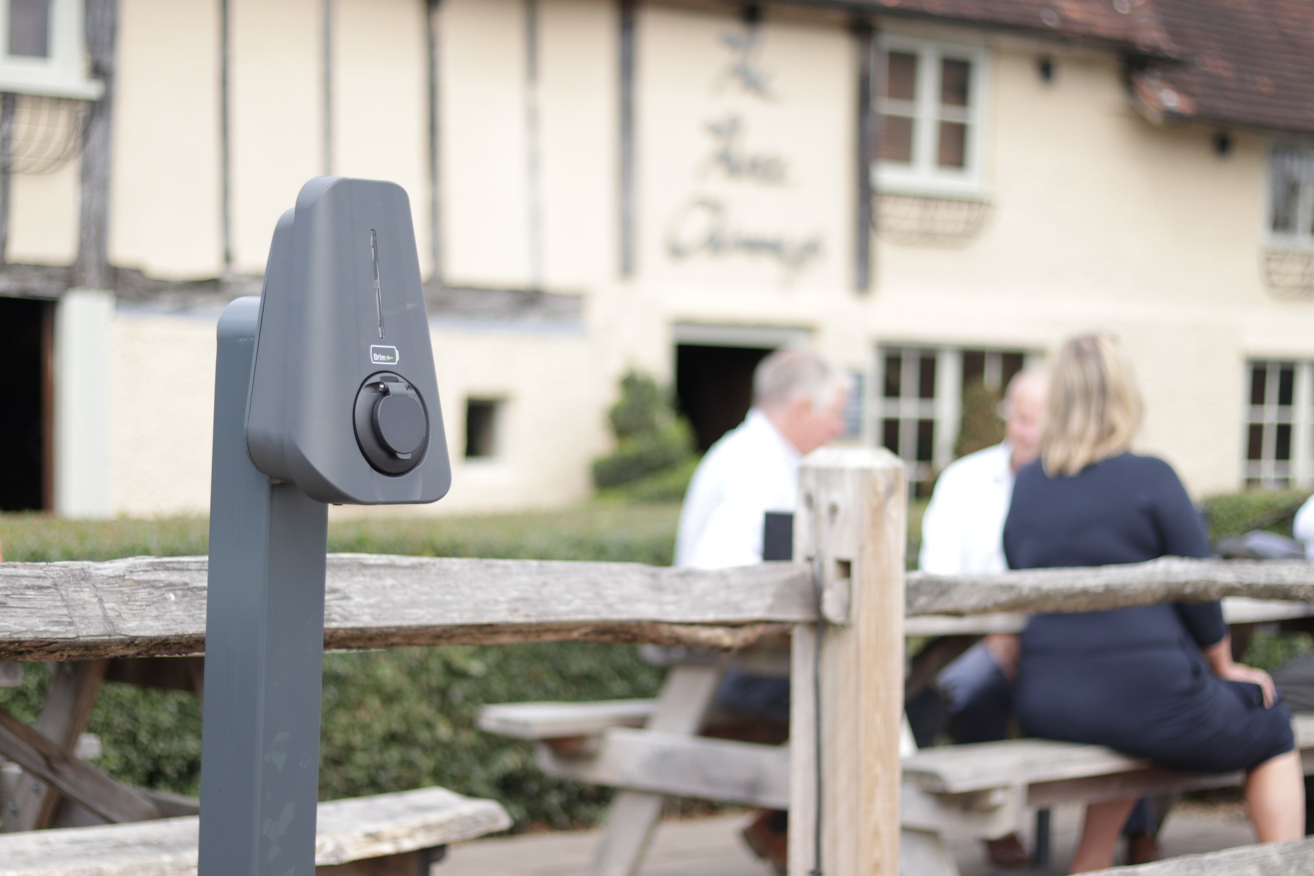 Brim Smart EV Charger in front of a country fence outside a blurred British tudor styled pub.