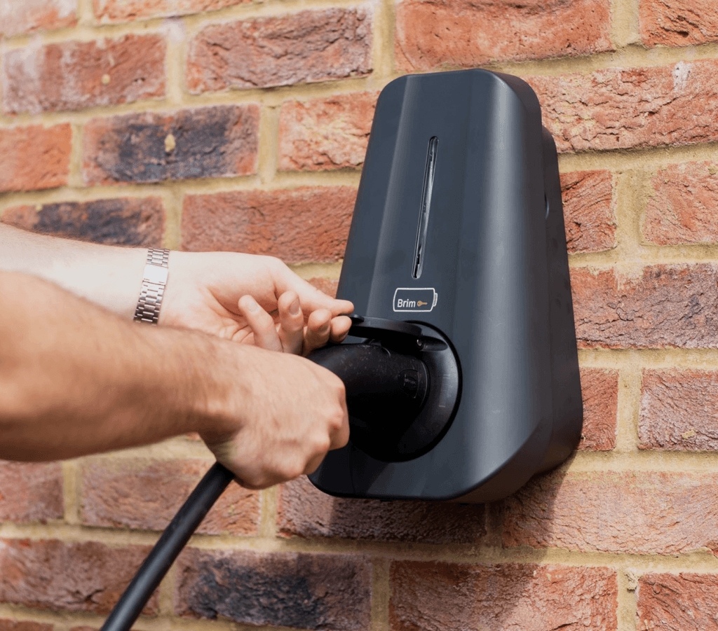 Person plugging charging cable into a Brim Smart EV Charger mounted on a brick wall.